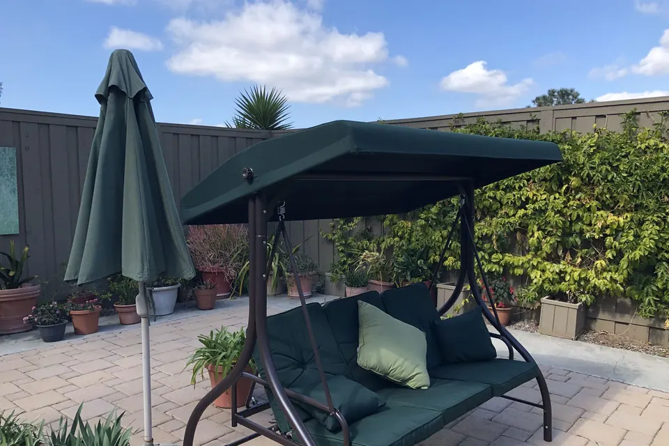 Green three-seat patio swing with canopy assembled in a backyard