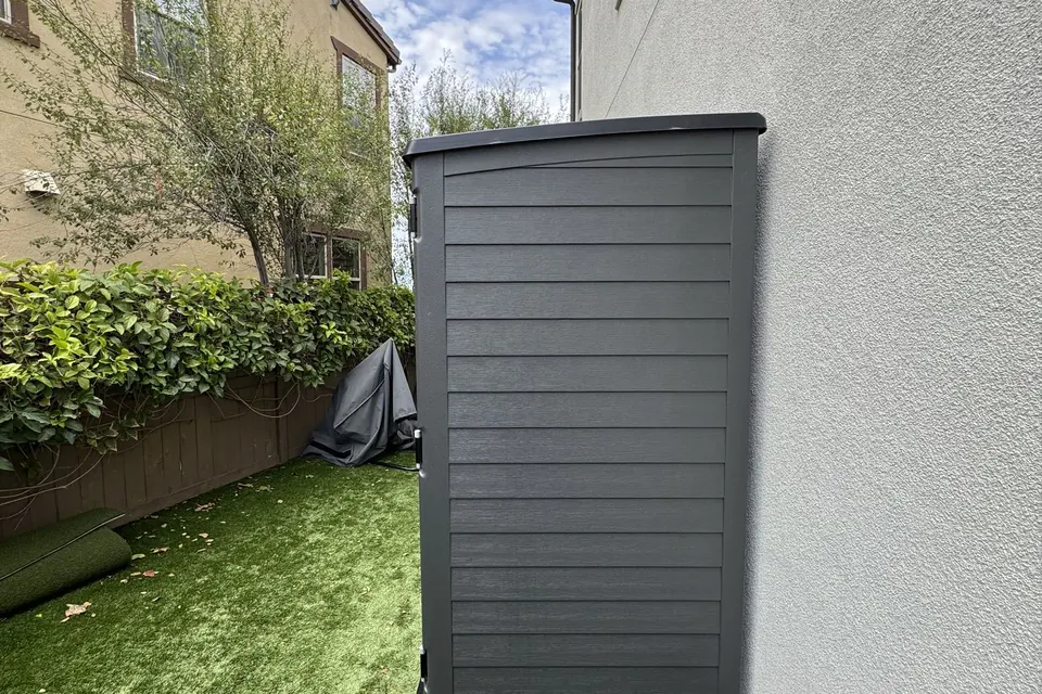 Grey resin storage shed assembled in a side yard