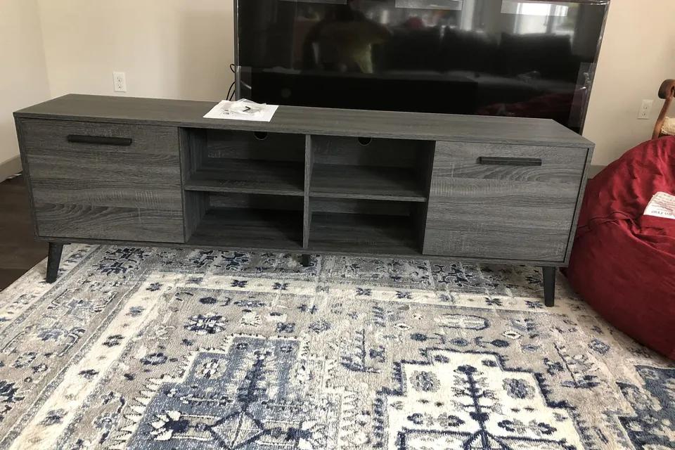 Grey TV console assembled with a TV on top, on a patterned rug